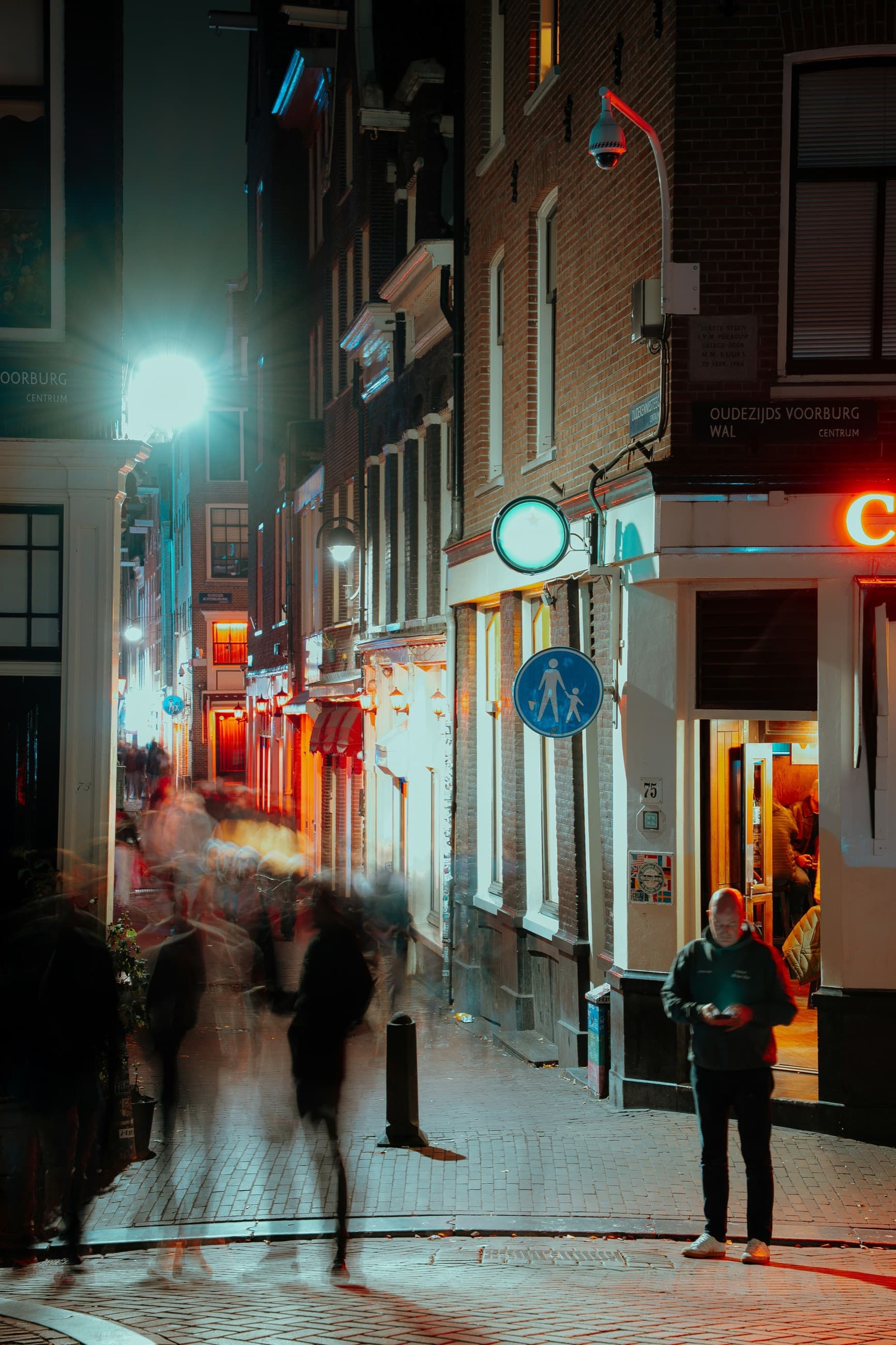 A night street with people passing beneath a surveillance camera